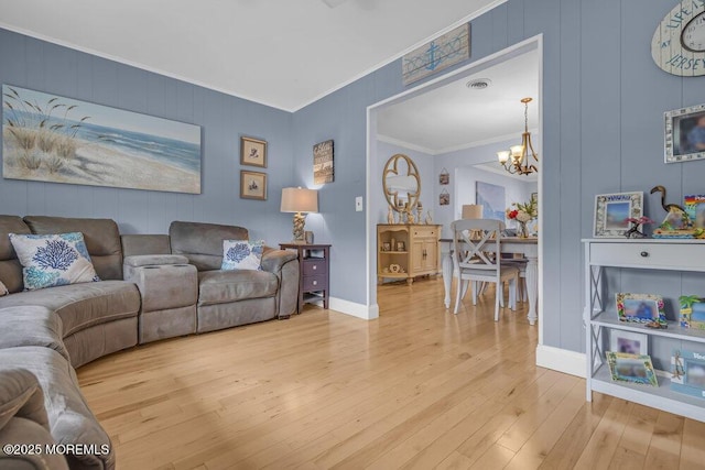 living room with an inviting chandelier, ornamental molding, light wood finished floors, and baseboards