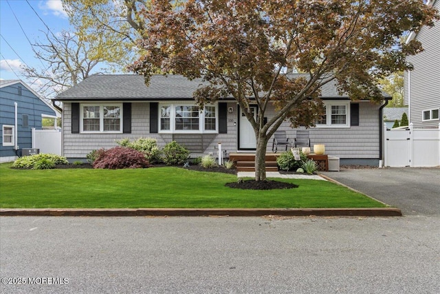 view of front of property featuring cooling unit, roof with shingles, fence, and a front yard