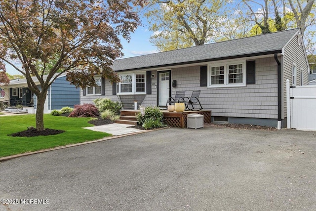 ranch-style house featuring covered porch, a shingled roof, and a front lawn