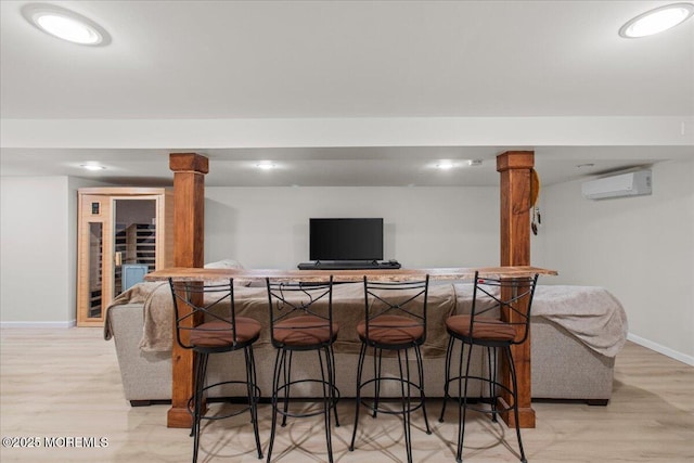 bar with a bar, an AC wall unit, baseboards, and light wood-style flooring