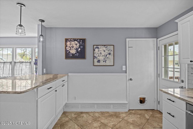 kitchen with white cabinets, a peninsula, light stone countertops, and decorative light fixtures