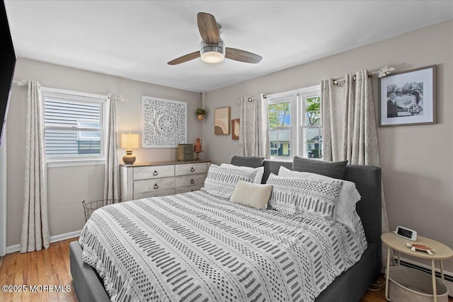 bedroom featuring light wood-style floors, a baseboard heating unit, baseboards, and multiple windows
