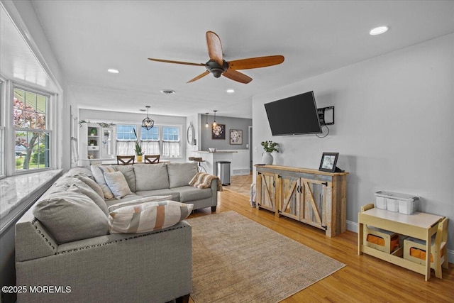 living area featuring recessed lighting, ceiling fan with notable chandelier, and light wood-style floors