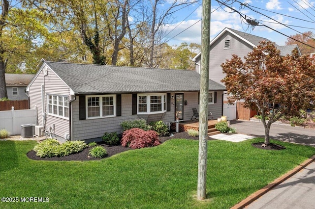 ranch-style house with central AC unit, roof with shingles, fence, and a front yard