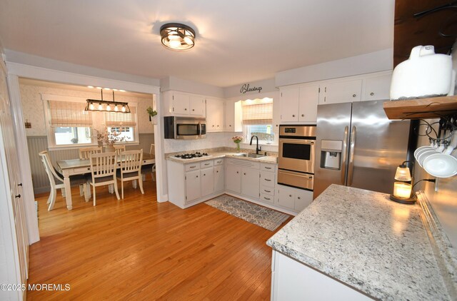kitchen featuring a sink, a warming drawer, light wood-style flooring, white cabinets, and appliances with stainless steel finishes