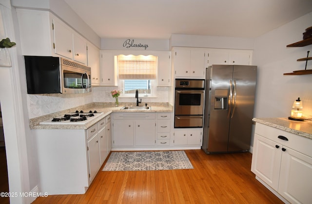 kitchen with appliances with stainless steel finishes, a warming drawer, light wood-style flooring, and a sink
