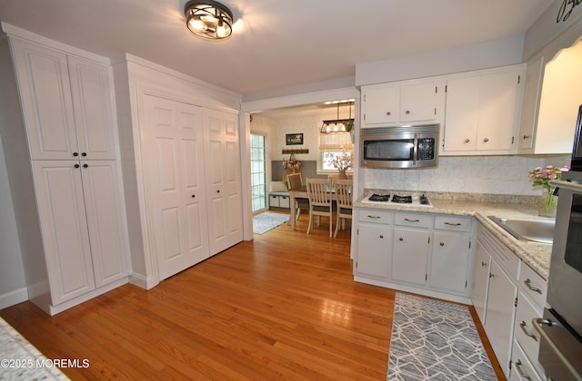 kitchen with stainless steel microwave, decorative backsplash, light countertops, white cabinets, and light wood-type flooring
