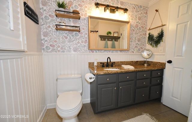 bathroom featuring toilet, tile patterned flooring, wallpapered walls, and a wainscoted wall