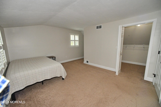 bedroom featuring light colored carpet, lofted ceiling, a closet, and visible vents