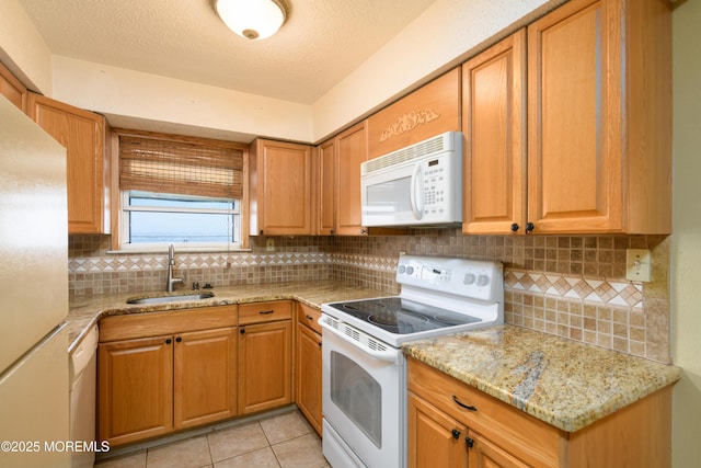 kitchen with a sink, white appliances, light stone counters, and backsplash