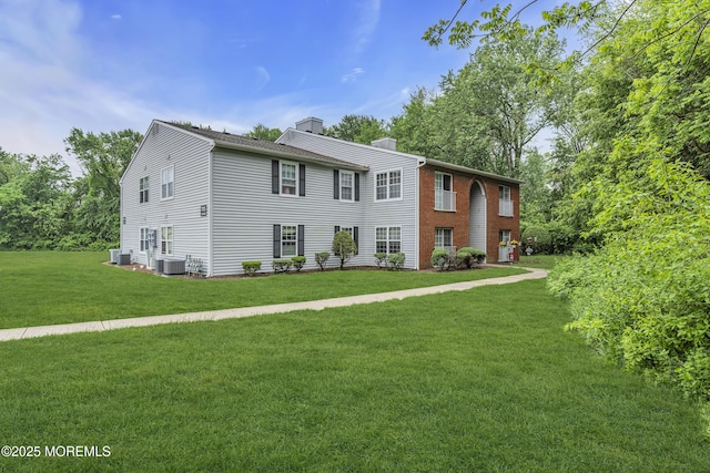 colonial-style house featuring a chimney, cooling unit, and a front lawn