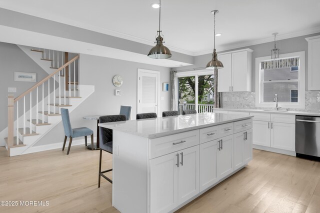 kitchen featuring stainless steel dishwasher, a sink, crown molding, a center island, and tasteful backsplash