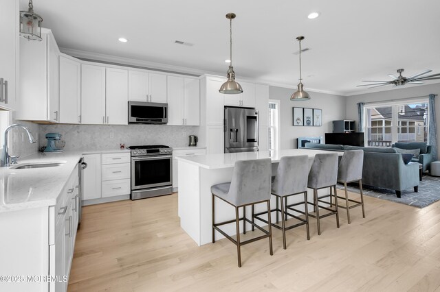 kitchen featuring appliances with stainless steel finishes, a sink, ornamental molding, light wood-style flooring, and open floor plan