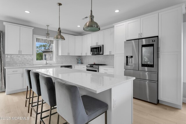 kitchen featuring stainless steel appliances, white cabinetry, light wood-style floors, a kitchen island, and ornamental molding