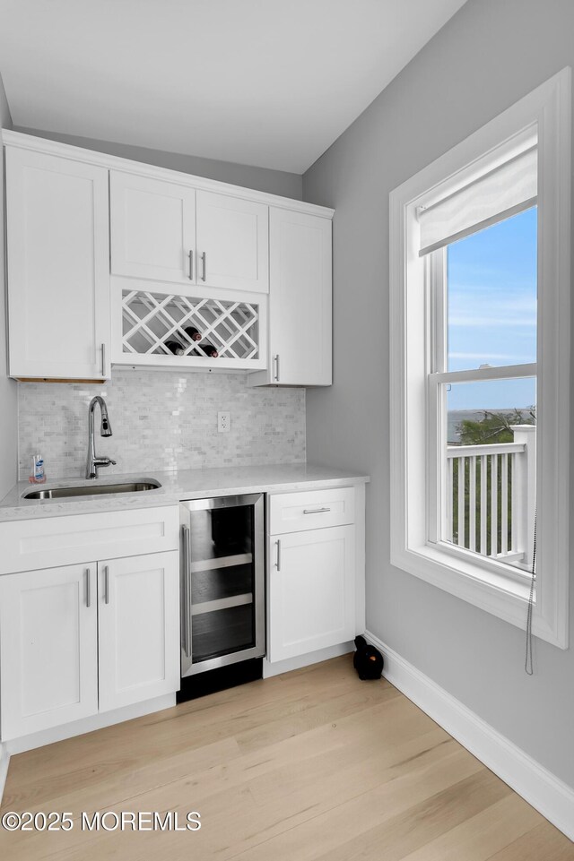 indoor wet bar with beverage cooler, tasteful backsplash, light wood finished floors, and baseboards