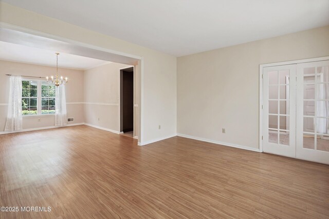 empty room with a chandelier, light wood-style flooring, and baseboards