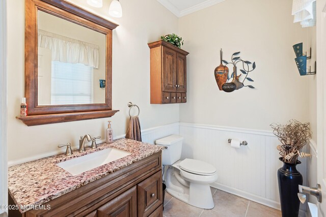 half bathroom with a wainscoted wall, ornamental molding, toilet, vanity, and tile patterned flooring