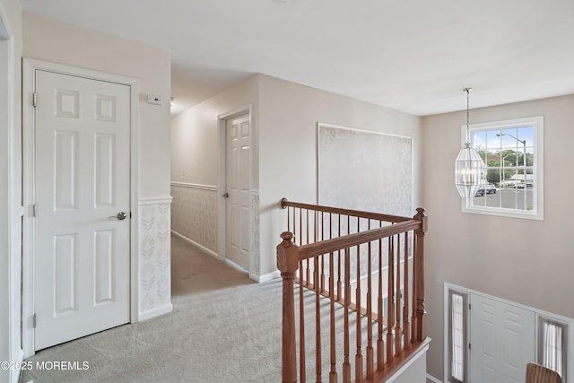 corridor with an upstairs landing, carpet flooring, a wainscoted wall, and a chandelier