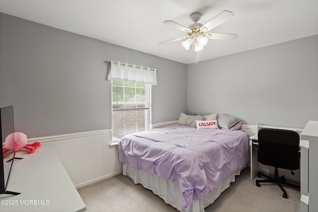 bedroom with a wainscoted wall, light carpet, and ceiling fan