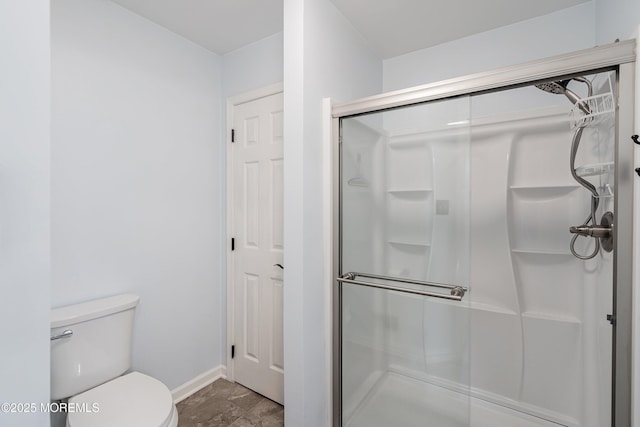 bathroom with a stall shower, toilet, and baseboards