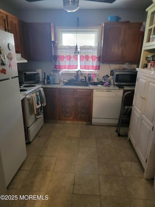 kitchen with a sink, white appliances, light countertops, and under cabinet range hood