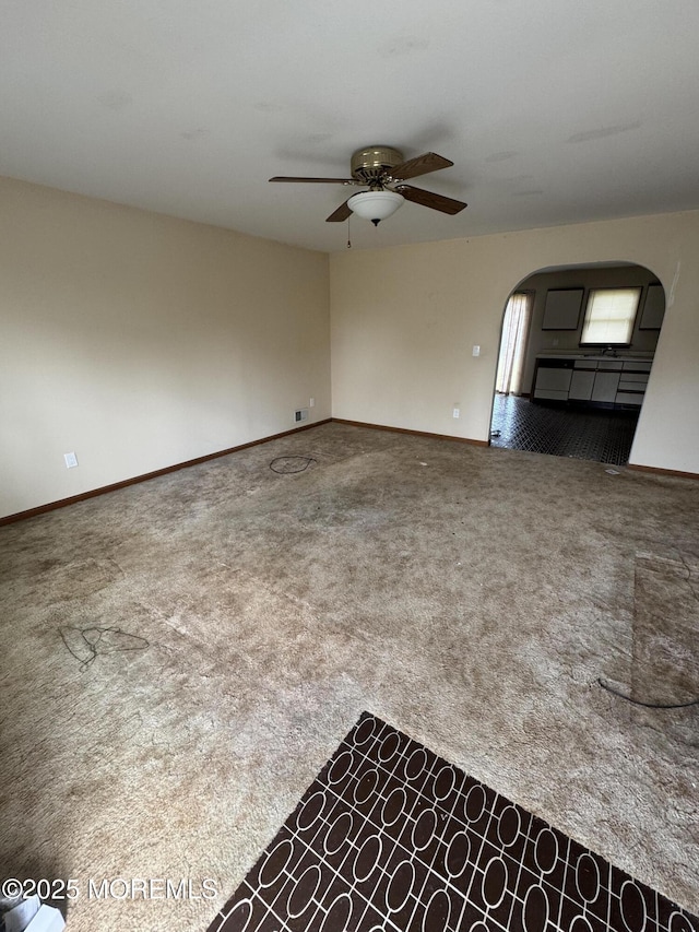 carpeted empty room featuring arched walkways, a ceiling fan, and baseboards