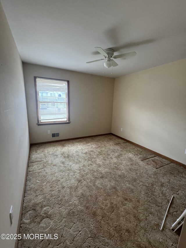 carpeted empty room with baseboards, a ceiling fan, and visible vents