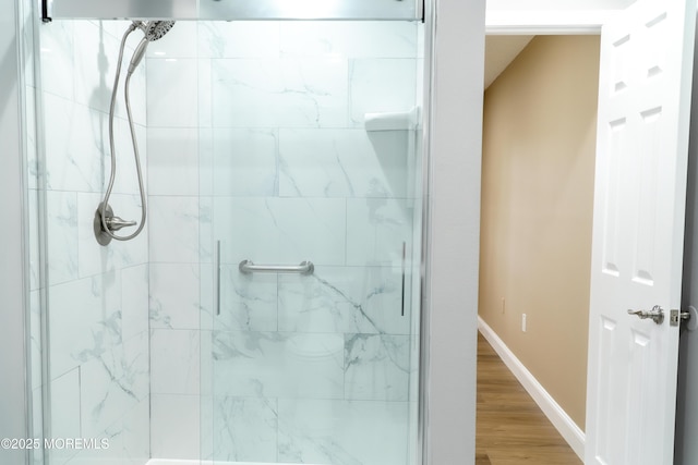 full bathroom with a stall shower, baseboards, and wood finished floors