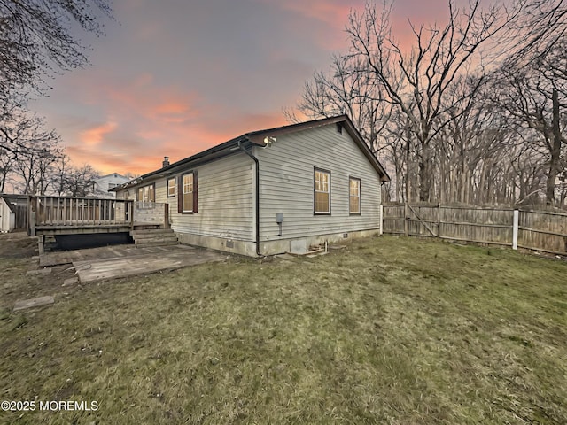 property exterior at dusk with a yard, a deck, a fenced backyard, and a patio