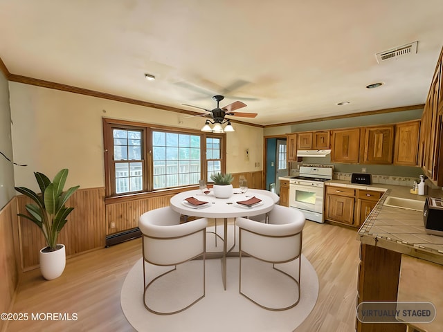 kitchen featuring brown cabinets, under cabinet range hood, tile counters, white gas stove, and wainscoting