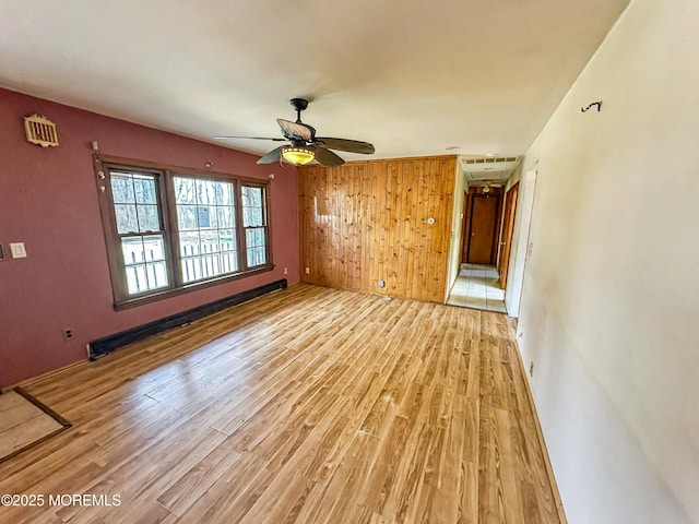 empty room featuring wood walls, visible vents, a baseboard radiator, a ceiling fan, and light wood-style floors