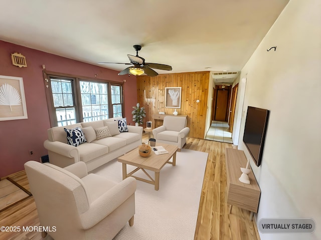living room featuring light wood finished floors, wood walls, visible vents, and ceiling fan