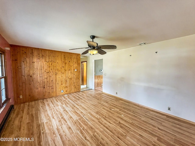 spare room featuring a ceiling fan, light wood-type flooring, visible vents, baseboards, and wooden walls