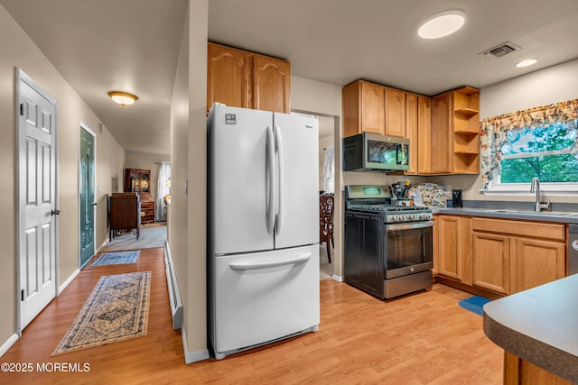 kitchen featuring stainless steel appliances, a sink, light wood-type flooring, and dark countertops
