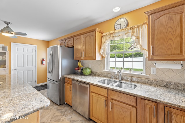 kitchen featuring appliances with stainless steel finishes, a sink, light stone counters, and tasteful backsplash