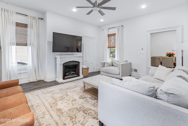 living room with ceiling fan, wood finished floors, a fireplace with raised hearth, recessed lighting, and baseboards