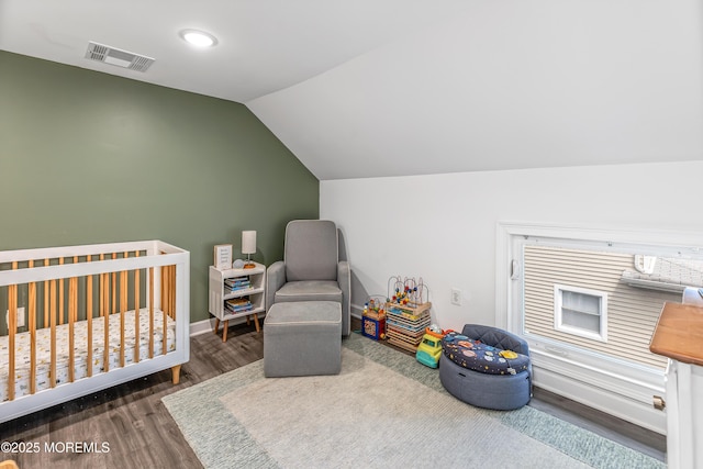 bedroom featuring lofted ceiling, a crib, wood finished floors, and baseboards