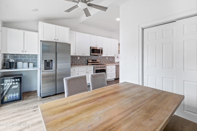 kitchen with appliances with stainless steel finishes, wine cooler, lofted ceiling, light countertops, and decorative backsplash