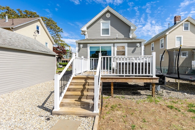 back of property with a trampoline, a deck, and stairway