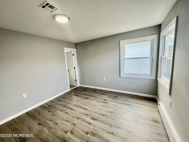 empty room featuring a baseboard radiator, wood finished floors, and baseboards