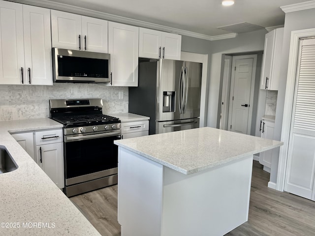 kitchen with stainless steel appliances, ornamental molding, white cabinetry, light wood-style floors, and light stone countertops