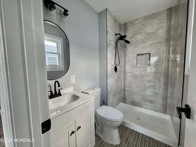 bathroom featuring toilet, a tile shower, vanity, and tile patterned floors