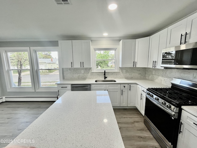 kitchen featuring appliances with stainless steel finishes, a sink, a baseboard heating unit, ornamental molding, and light stone countertops