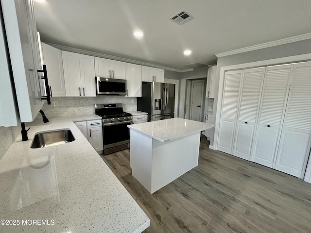 kitchen with appliances with stainless steel finishes, ornamental molding, tasteful backsplash, a kitchen island, and light stone counters