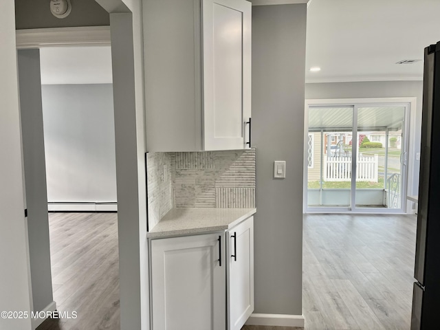 kitchen with baseboard heating, decorative backsplash, ornamental molding, white cabinetry, and light wood-style flooring