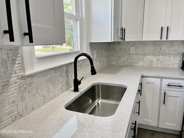 kitchen featuring a sink, decorative backsplash, white cabinetry, and light stone countertops