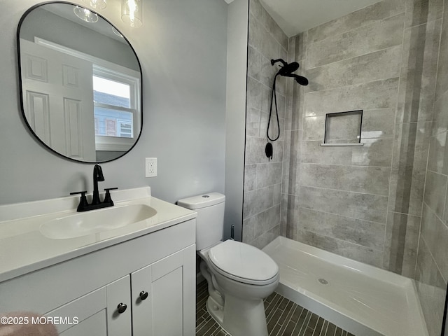 bathroom featuring toilet, vanity, tiled shower, and tile patterned floors