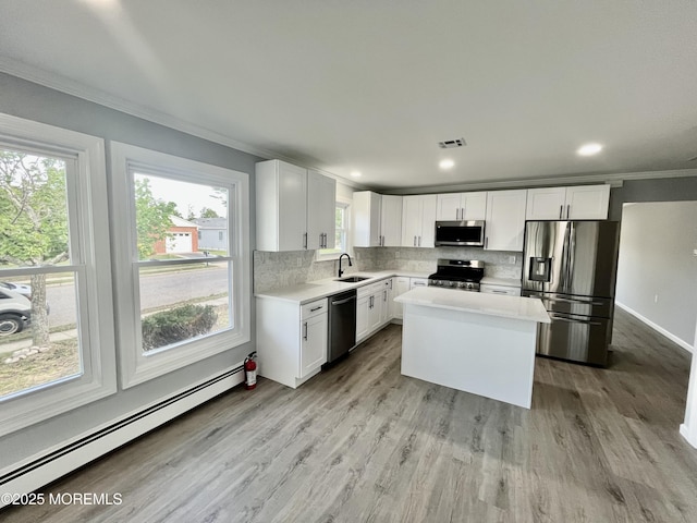 kitchen featuring stainless steel appliances, a baseboard heating unit, a sink, ornamental molding, and light countertops