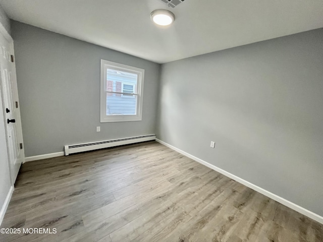 unfurnished room with baseboard heating, wood finished floors, and baseboards