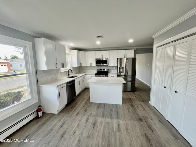 kitchen featuring stainless steel appliances, crown molding, a baseboard radiator, backsplash, and healthy amount of natural light